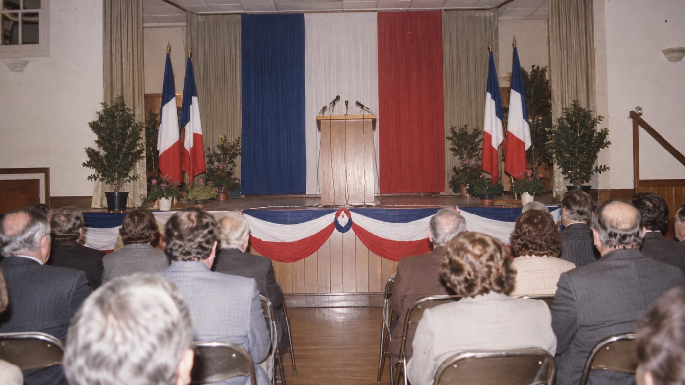 Salle des fêtes de village avec estrade tricolore et chaises pliantes
